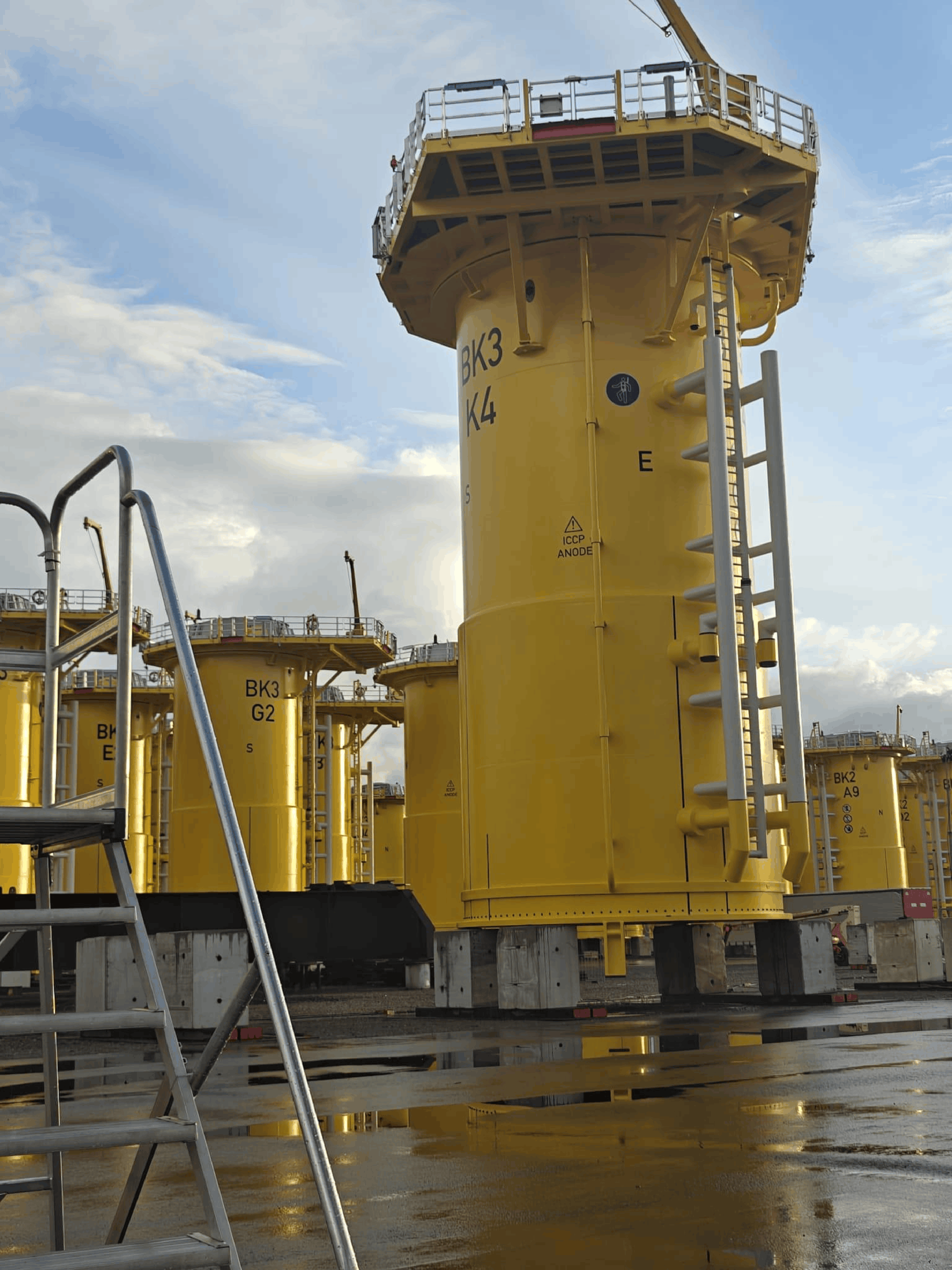 Large yellow offshore monopile foundations staged in an industrial yard