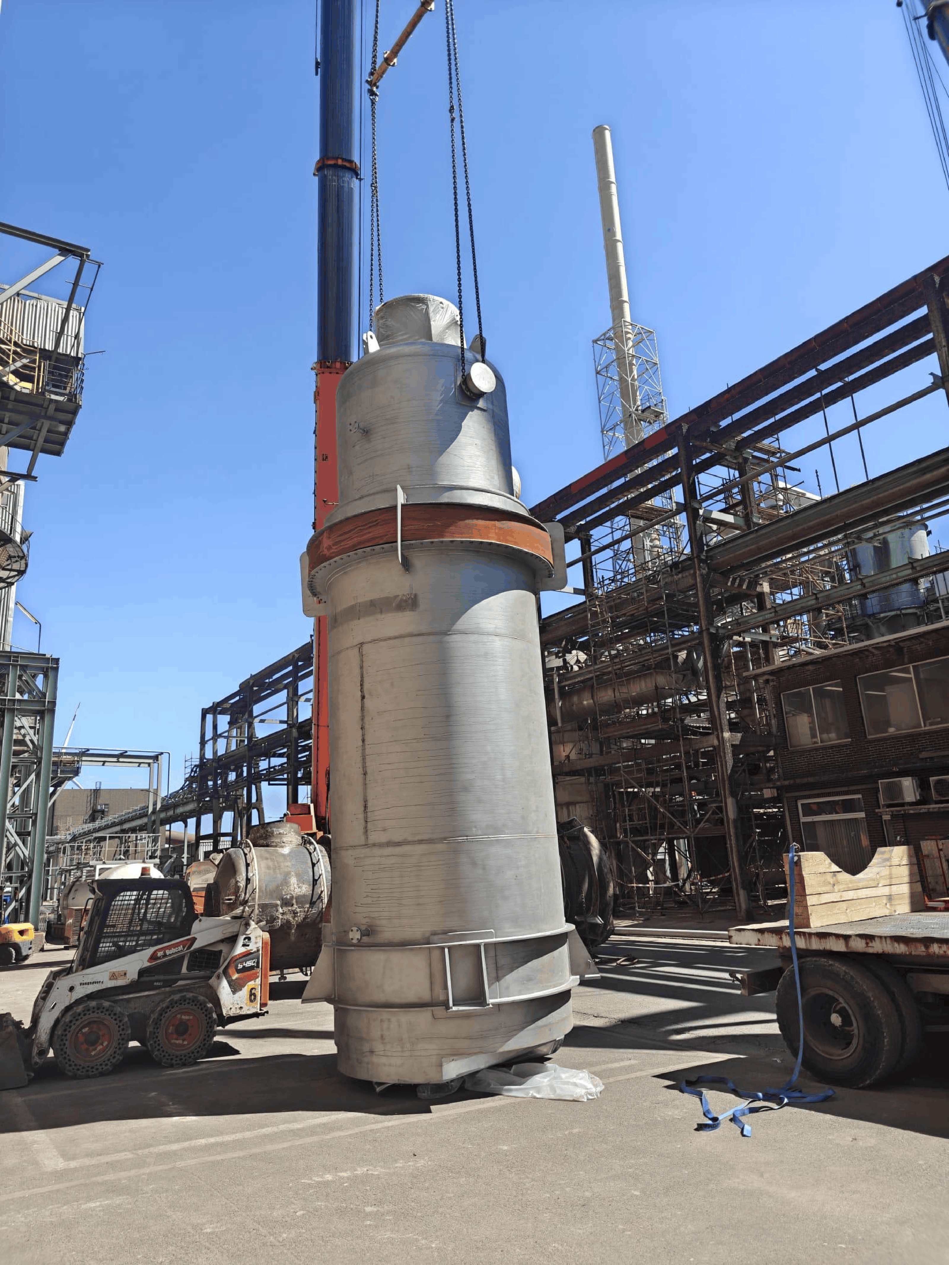 Industrial vessel being lifted by crane at a large petrochemical refinery