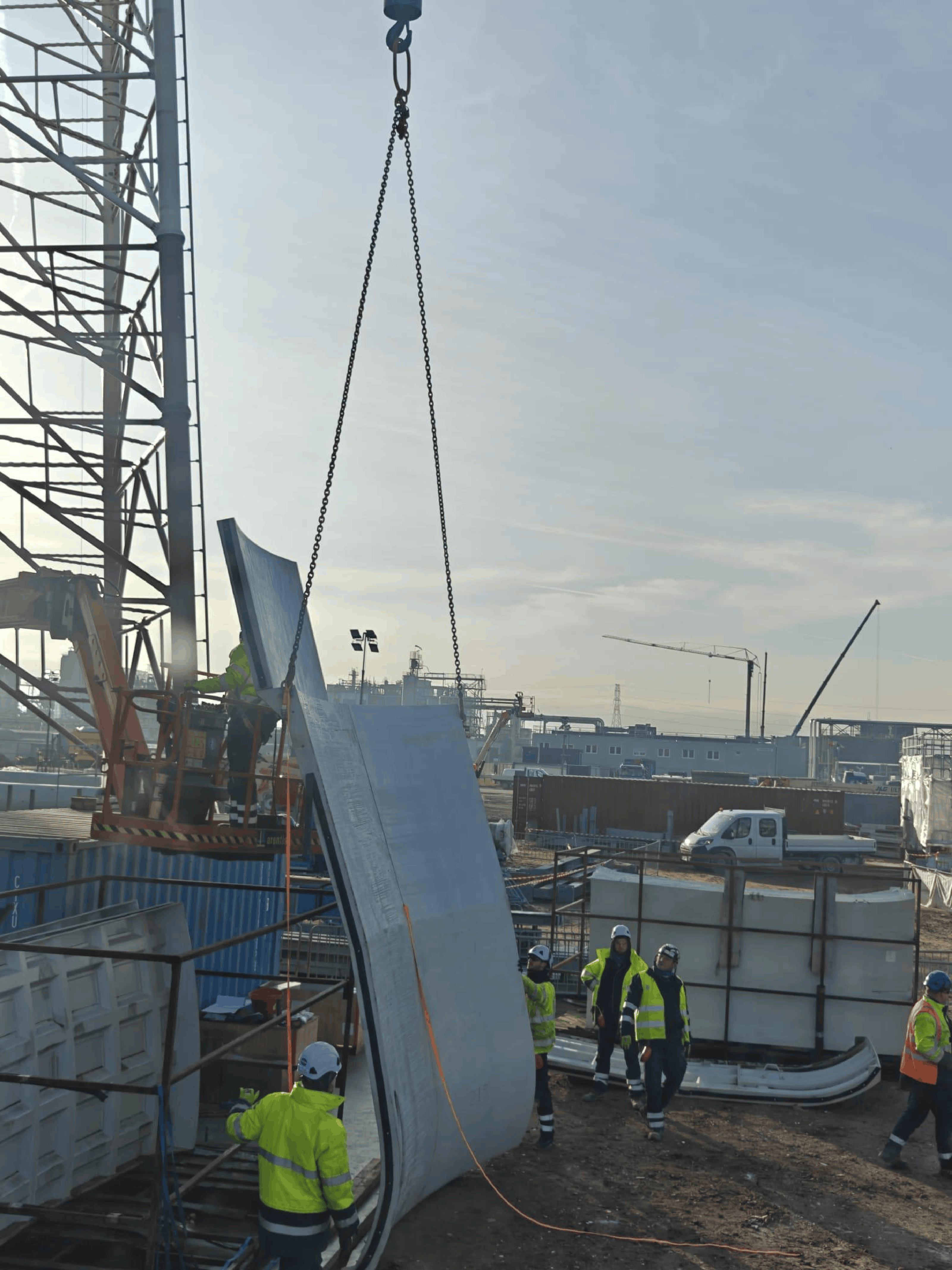 PPE-equipped site workers guiding a large steel component being hoisted at an industrial lifting zone