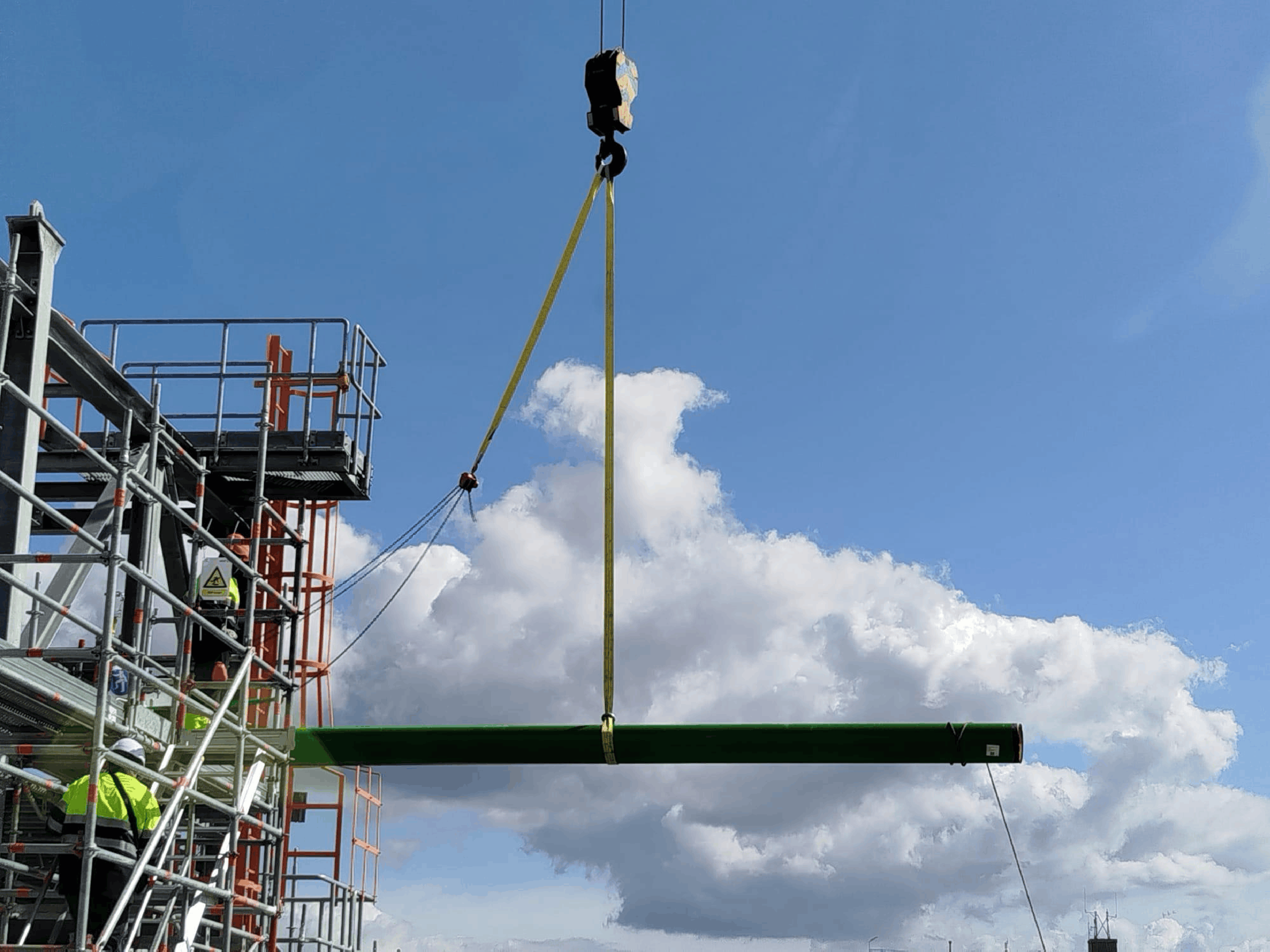 Heavy green steel component suspended on crane hook at industrial site